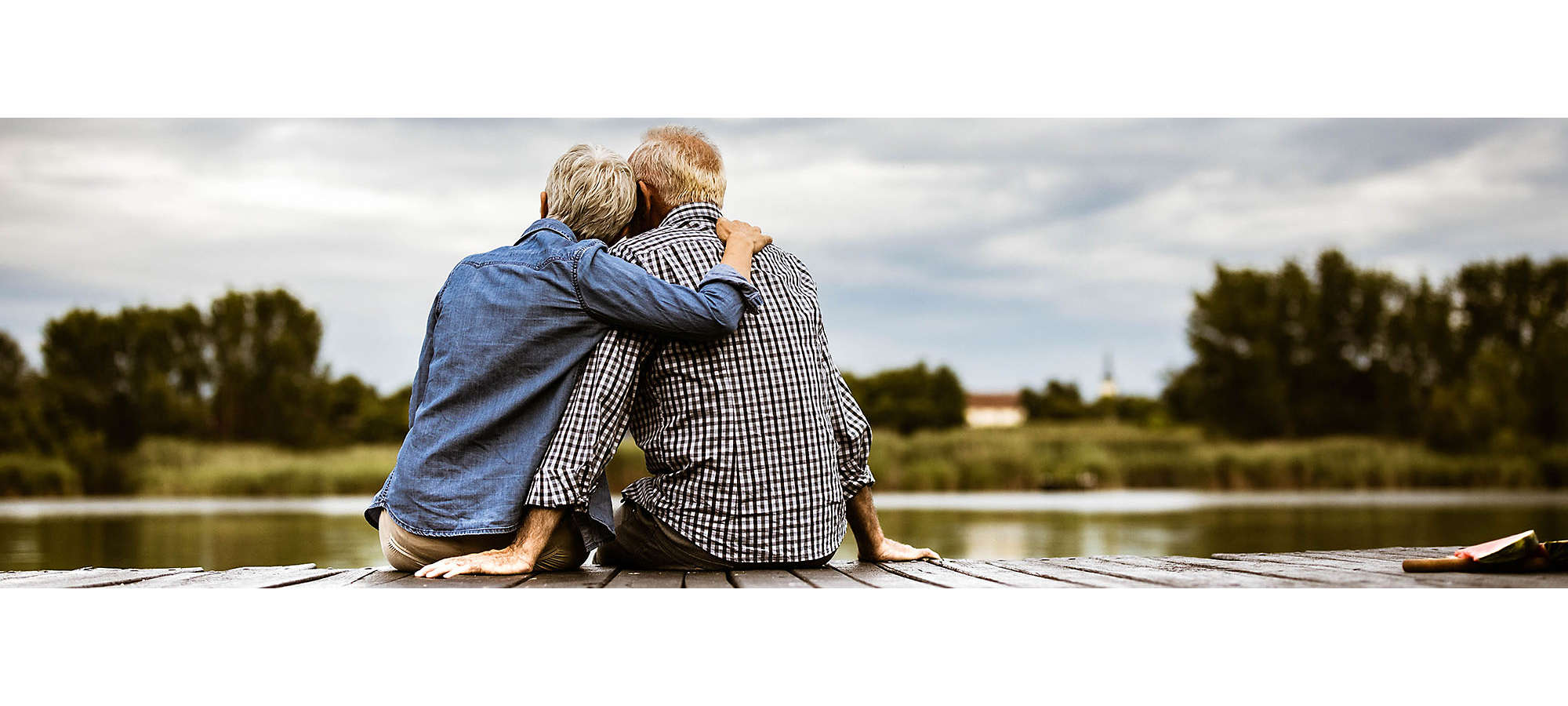 A mature couple outside sitting on a dock overlooking a lake.