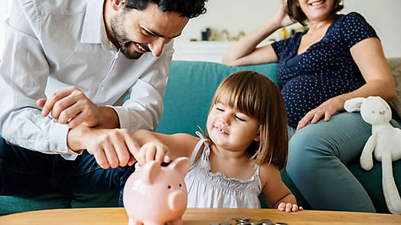 A father helping his daughter put change in a piggy bank