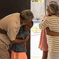 Grandparents hugging their grandchildren by the front door of a house.
