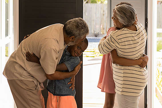 Grandparents hugging their grandchildren by the front door of a house.