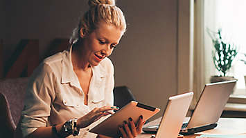 A woman sitting at her desk looking at something on her tablet.