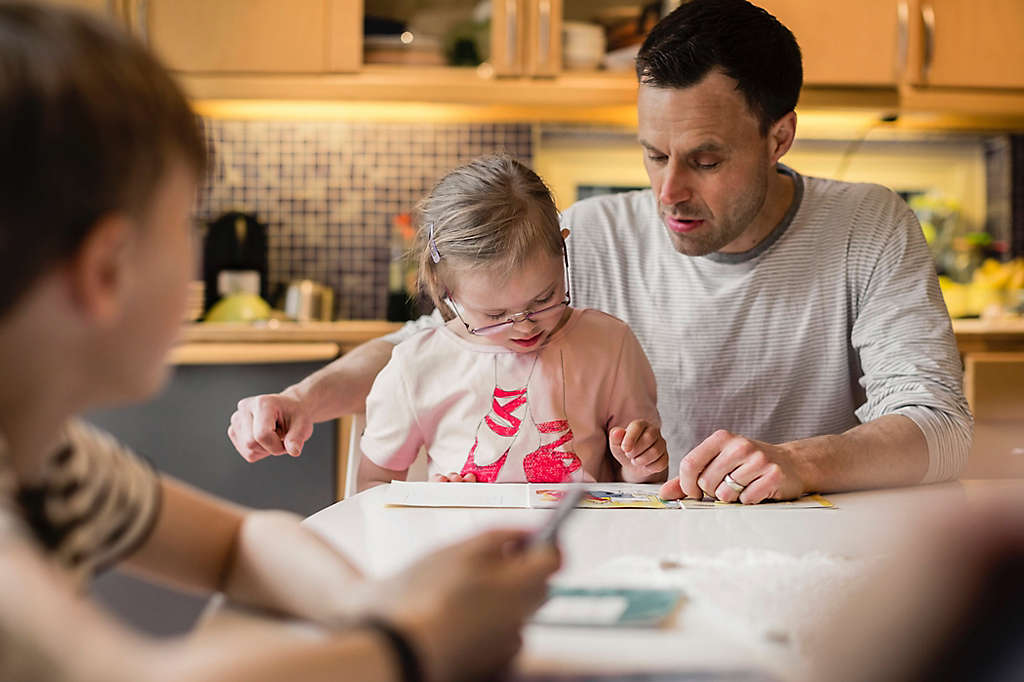 Father teaching daughter with son in foreground at home