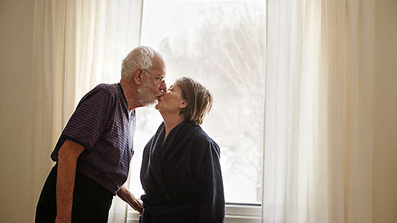 Senior couple kissing next to window 