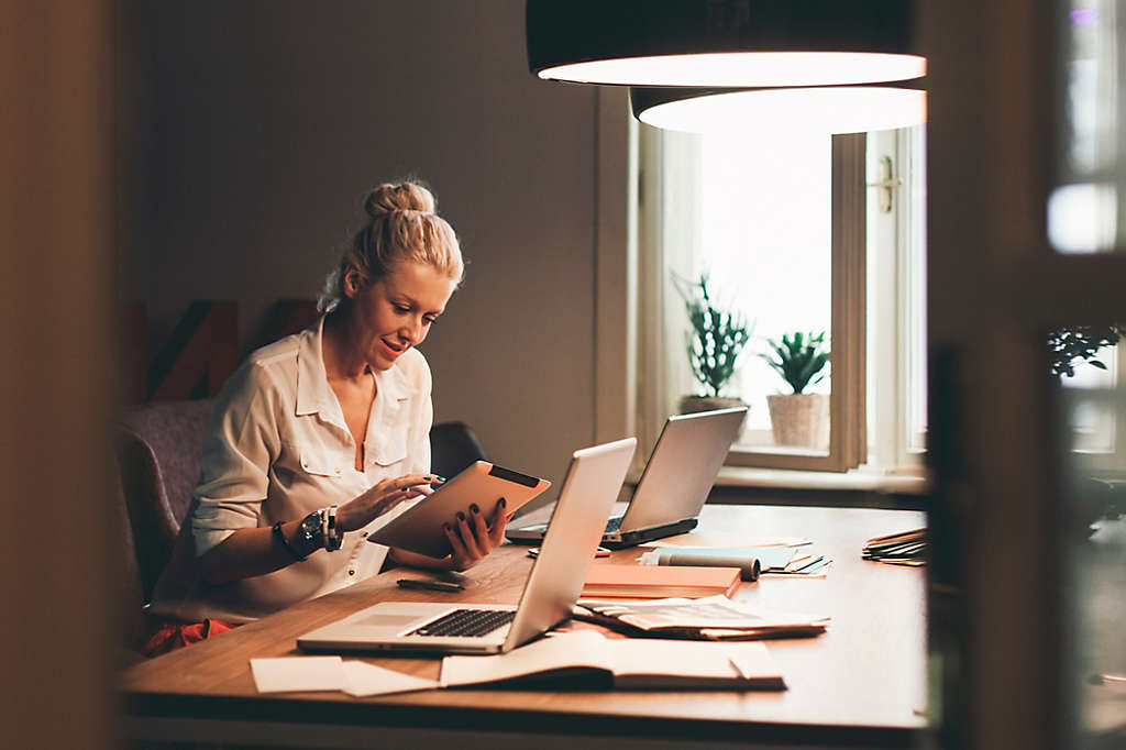 Woman at her desk with tablet and 2 laptops researching dividends.