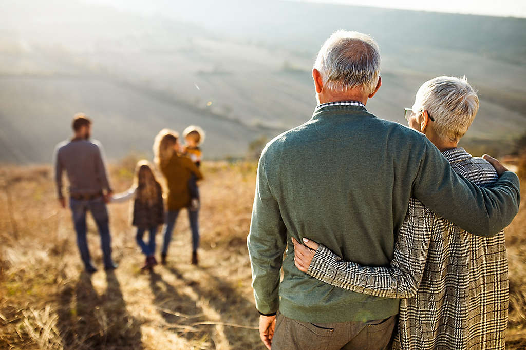 An older couple outside embracing looking at their children and grandchildren.