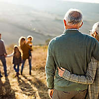 An older couple outside embracing looking at their children and grandchildren.