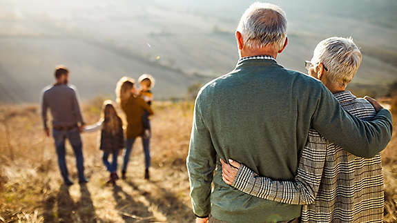 An older couple outside embracing looking at their children and grandchildren.