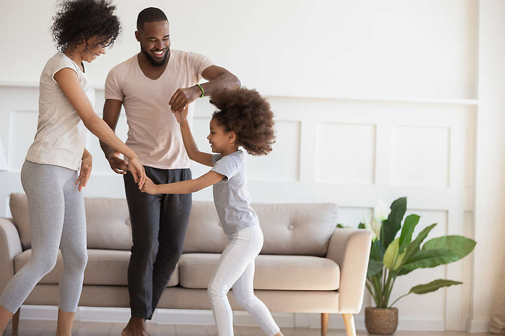 A mother and father dancing with their daughter in the living room.