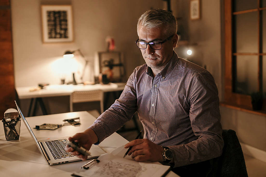 An older man looking over documents while working on his computer.