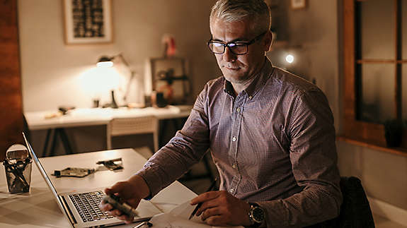 An older man looking over documents while working on his computer.