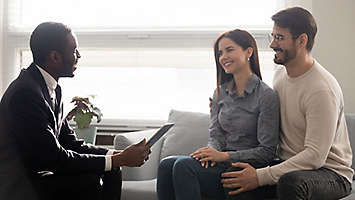 An agent sitting down and talking with a young couple.