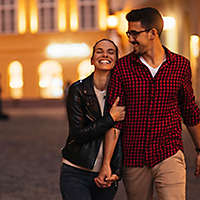 A young couple walking down a street holding hands and smiling.