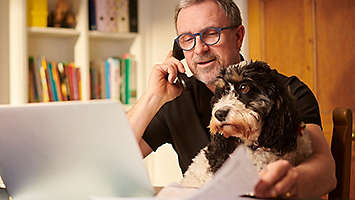 Man on the phone, sitting with his dog.