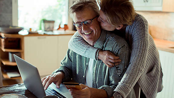 A mature couple kissing while the husband is using his computer.