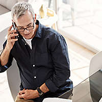 A mature man on the phone and working on his computer.