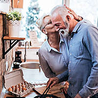 A mature woman kissing a mature man while he's cooking breakfast.