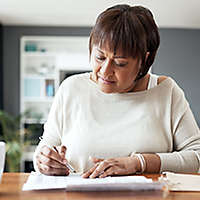 A mature woman sitting at a table with a calculator writing on papers.