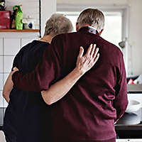 An older couple embracing in the kitchen.