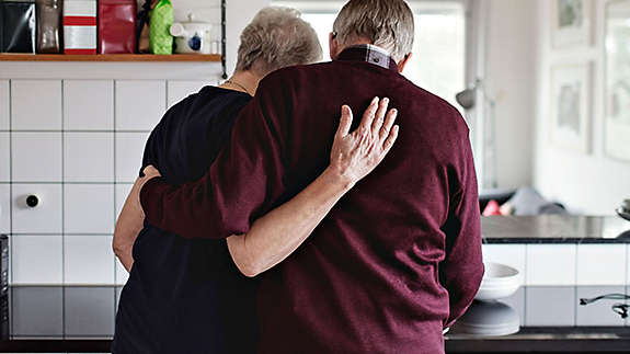 An older couple embracing in the kitchen.