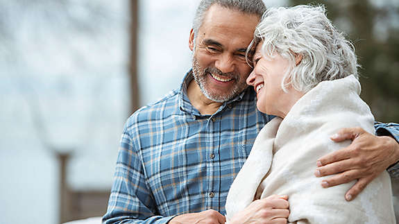 An older couple embracing and smiling on a park bench.
