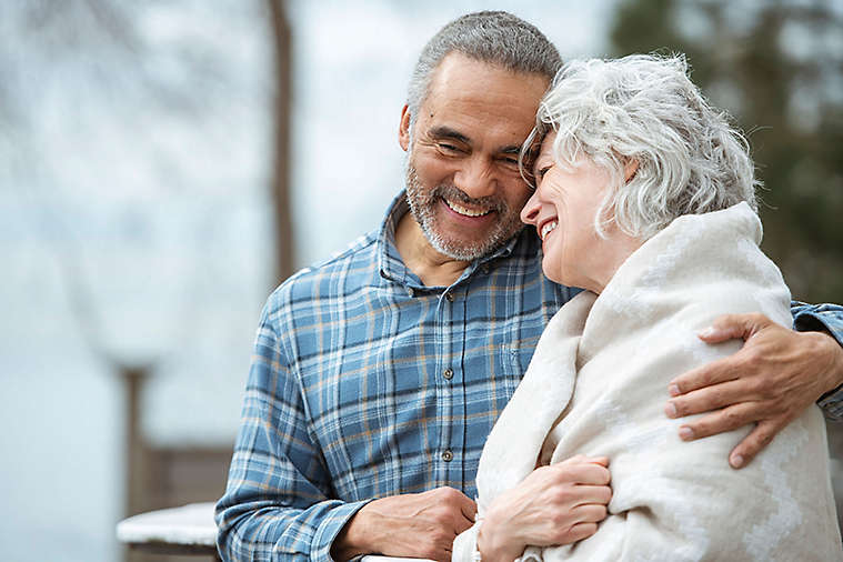 An older couple embracing and smiling on a park bench.