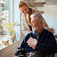 A young woman standing behind an older man in a wheelchair.