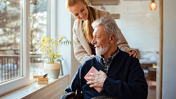 A young woman standing behind an older man in a wheelchair.