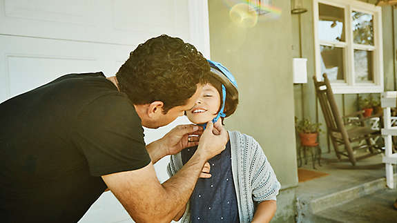 Father helping daughter buckle helmet before riding scooter