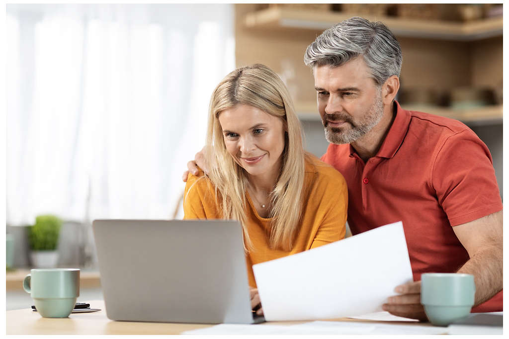 A couple looking at their laptop and holding a piece of paper