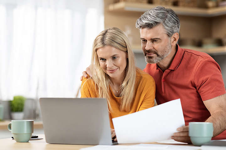 A couple looking at their laptop and holding a piece of paper