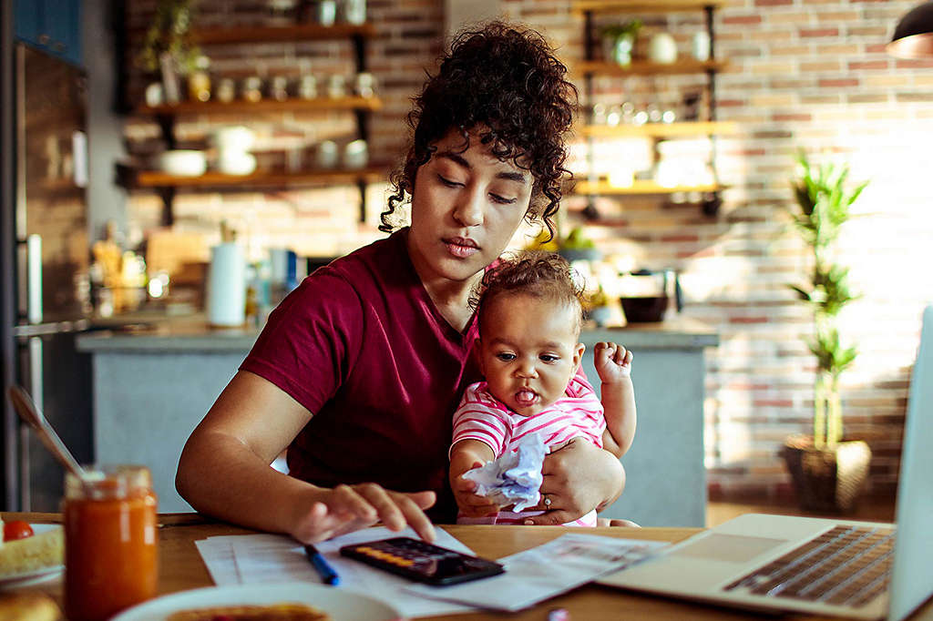 Woman sitting at desk holding baby while tapping on phone. 