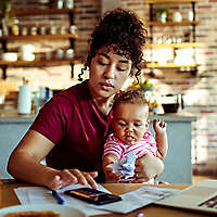 Woman sitting at desk holding baby while tapping on phone. 