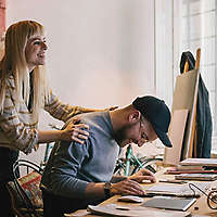 Man working on computer while woman looks over his shoulder. 