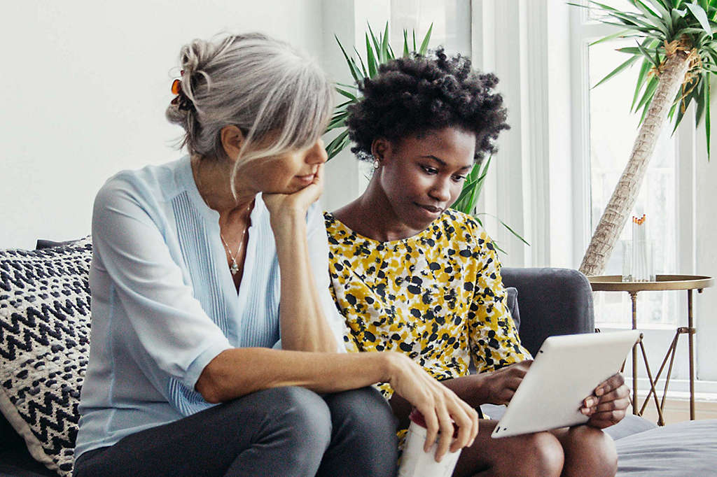 Two women sitting on couch looking at tablet together.