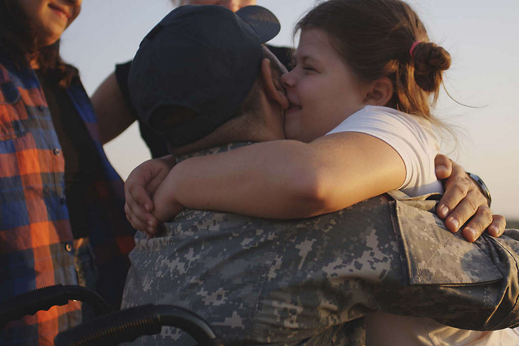 Father in army jacket embracing daughter.