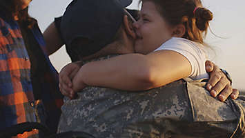 Father in army jacket embracing daughter.