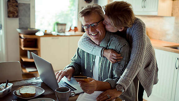 Man working on computer while wife gives him a kiss on the cheek.