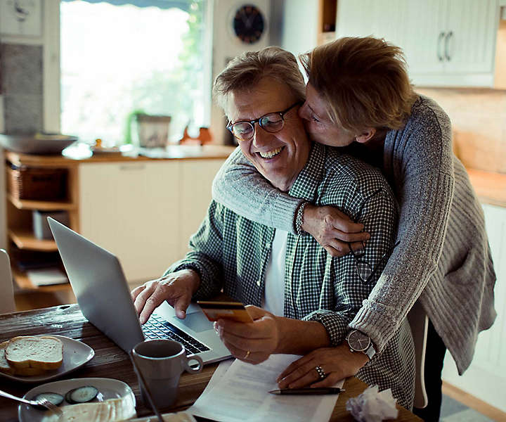 Man working on computer while wife gives him a kiss on the cheek.