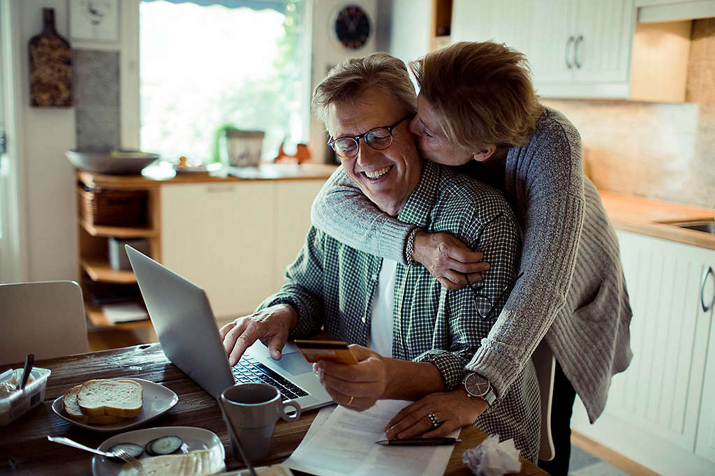 Man working on computer while wife gives him a kiss on the cheek.