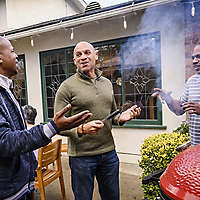 Three men talking while grilling at a barbecue. 