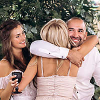 Woman hugging couple while holding drinks and celebrating.