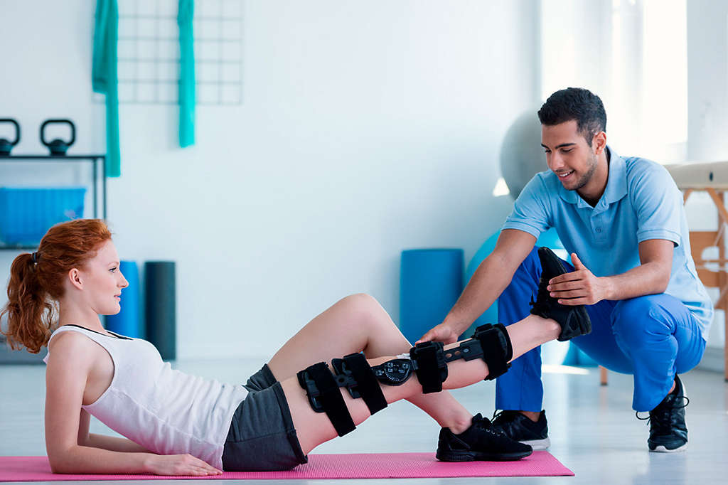 Woman with leg injury on mat and smiling doctor during treatment in the hospital