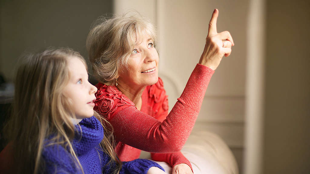 Retiree smiling and holding a small child while pointing off screen  as if showing them something in the distance