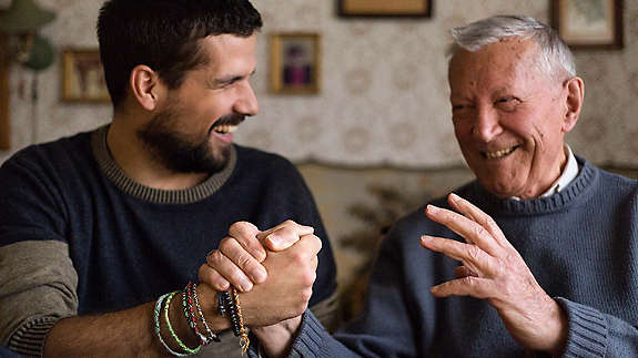 Laughing man holding hands with his smiling grandfather 