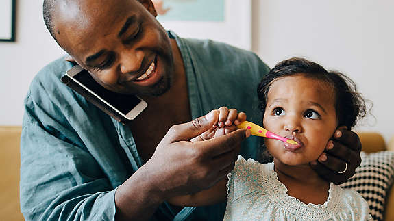 Parent brushing a child's teeth while using the phone