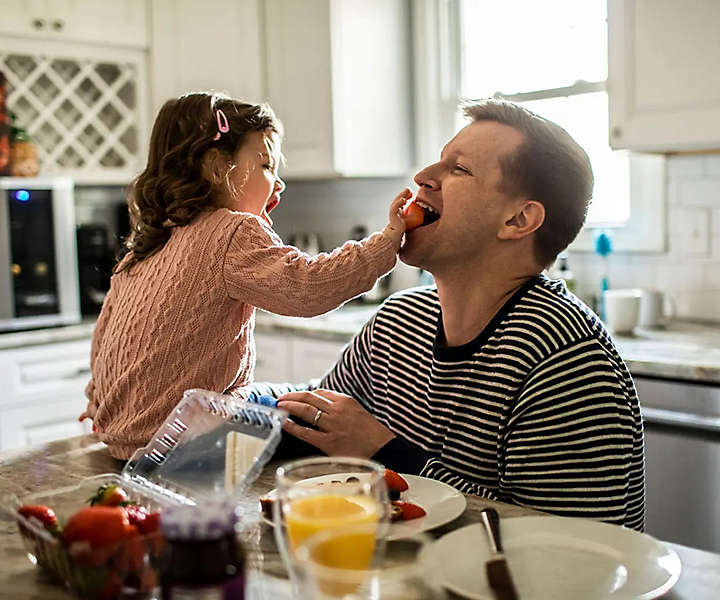 Toddler feeding father in kitchen