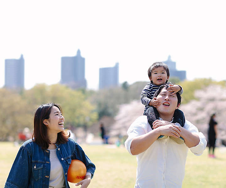 A father carrying a toddler on his shoulders while the child’s mother walks next to them in a city park