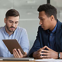 Two business people collaborating at a work table with electronics