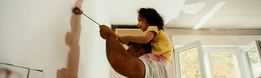 Father painting a room with his young daughter on his shoulders
