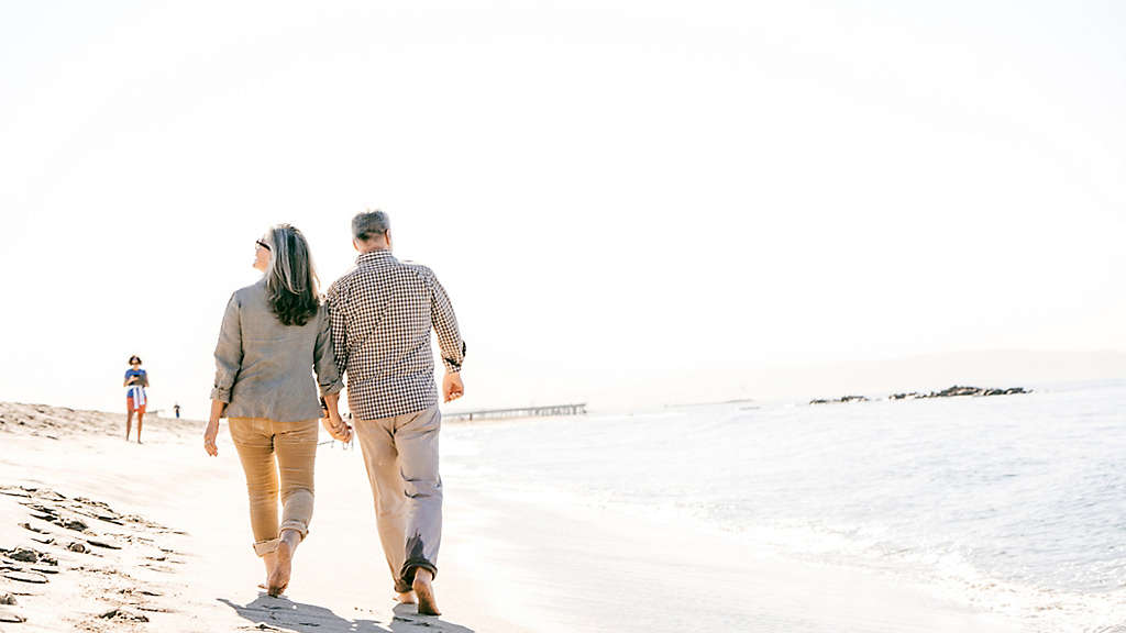 Middle aged couple walking hand in hand barefoot on the beach